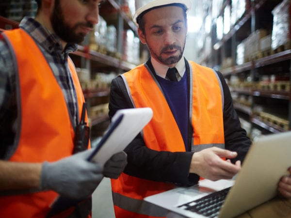 Businessman showing data in laptop to warehouse worker